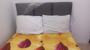 A bed with a headboard, two white pillows, and a bedspread with a pattern of red and yellow shapes. - OYO 95179 Namira Guest House Syariah (Kembaran)