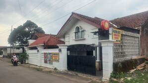 A house with a tiled roof, a gated entrance, and a sign advertising a business. - OYO 95179 Namira Guest House Syariah (Kembaran)