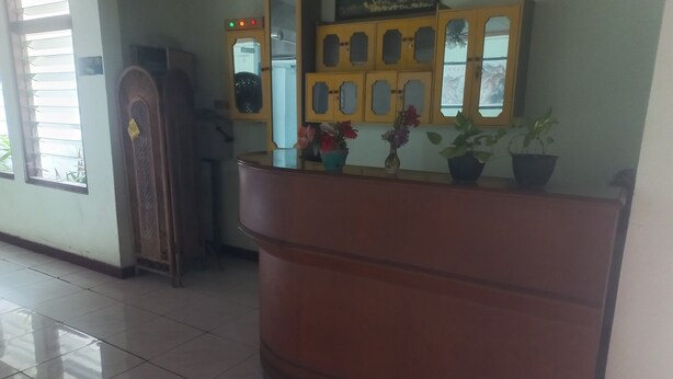 A reception area with a wooden counter, potted plants, and a window with blinds. - OYO 95179 Namira Guest House Syariah (Kembaran)