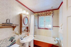 Un bagno d'epoca con una vasca piedi di leone, un lavabo su piedistallo e uno specchio con cornice decorativa.