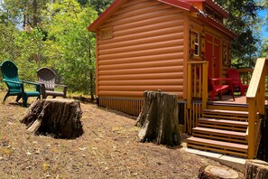 Eine Holzhütte mit Veranda, grünen und roten Adirondack-Stühlen und einer Holztreppe, die zum Eingang führt.