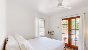 Un dormitori amb un llit, un ventilador de sostre, una finestra i una porta que dóna a un espai exterior.