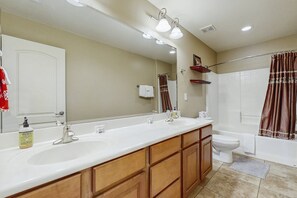 A bathroom with a large mirror, two sinks, a toilet, and a shower.
