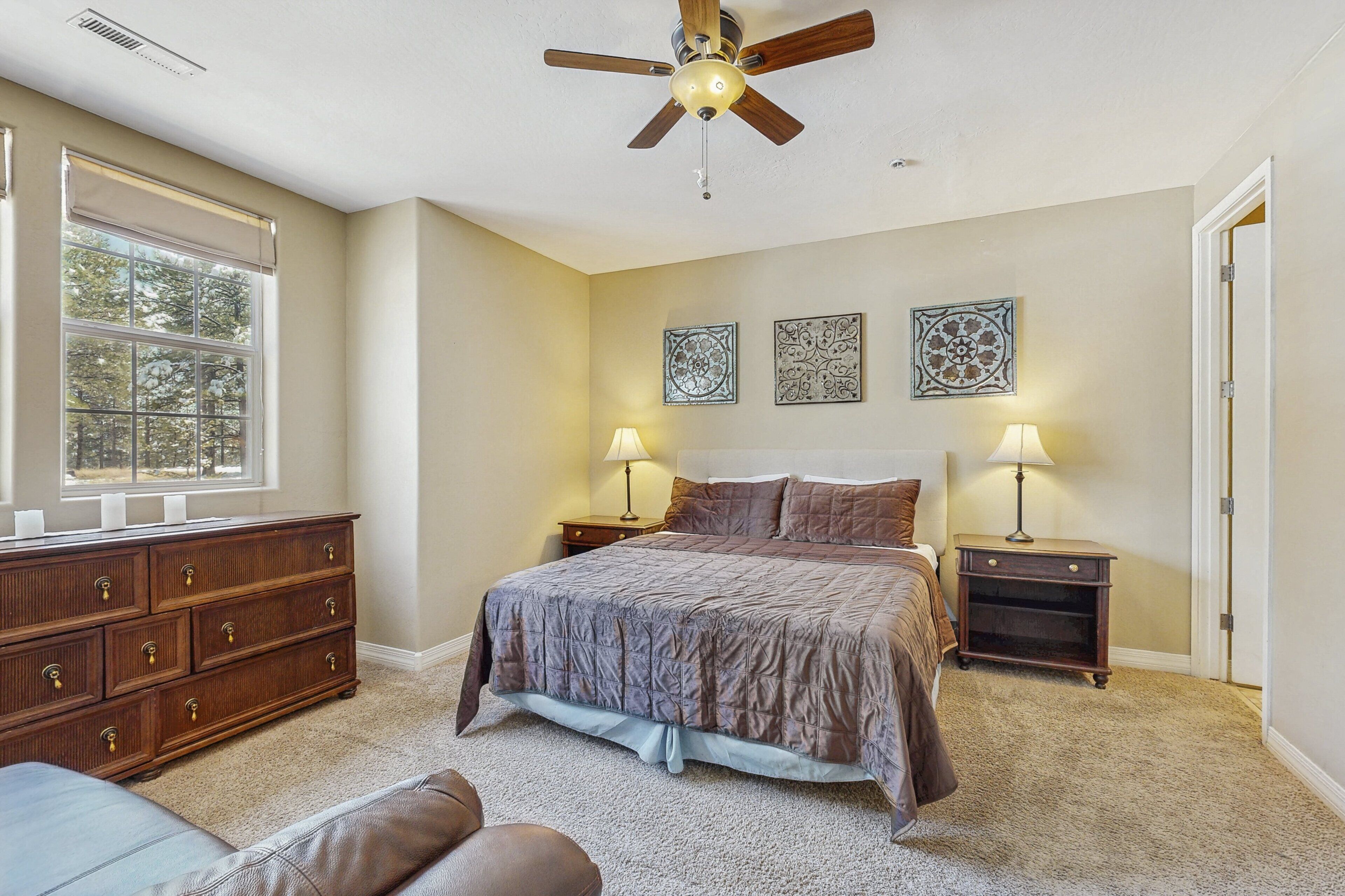 A bedroom with a bed, two bedside tables, a ceiling fan, a window, a dresser, and decorative wall art.
