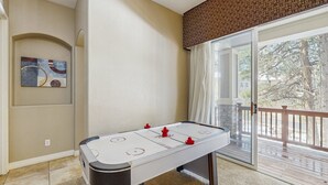 Una habitación con una mesa de fútbol de mesa, un cuadro en la pared y un amplio ventanal corredero que da a una terraza exterior.