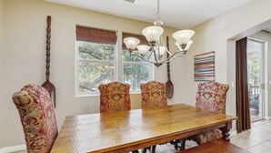 Comedor con mesa de madera, cuatro sillas tapizadas, una araña y ventana con vista a árboles.
