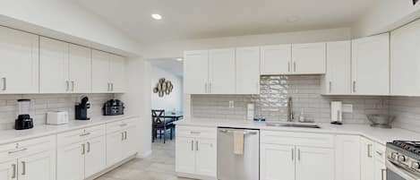 A modern kitchen with white cabinetry, a dishwasher, a coffee maker, and a stove.