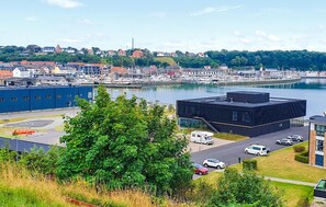 En småbåtshamn med båtar, en modern byggnad och utsikt över en stad med hus och grönområden.
