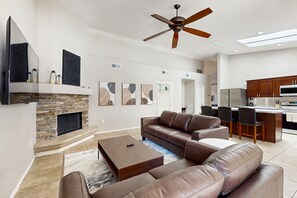 A spacious living room with a stone fireplace, leather sofas, a coffee table, and a ceiling fan. - Oasis in Sunny Scottsdale—where comfort, games, and poolside relaxation. (Scottsdale)