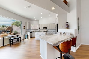 Una cocina amplia con armarios blancos, una isla grande con taburetes de bar y vistas al exterior.