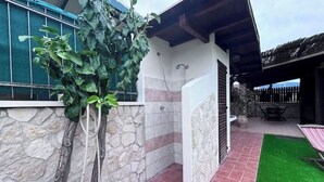 Een buitendouchegedeelte met stenen muren, een betegelde vloer, een kunstgrasveldje en een houten pergola.