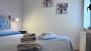 Een opgemaakt bed met gevouwen handdoeken, een blauw hoofdeinde en twee bloemschilderijen aan de muur.