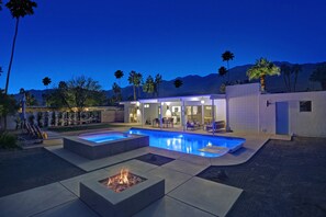 A modern outdoor pool area with a fire pit, seating, and a house in the background. - Mid-Century Modern Meiselman Home with Backyard Oasis, Pool & Spa (Palm Springs)