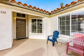 A covered porch with a door, two windows, and two chairs. - Island-inspired condo with olf course & mountain view & pool access (Palm Desert)