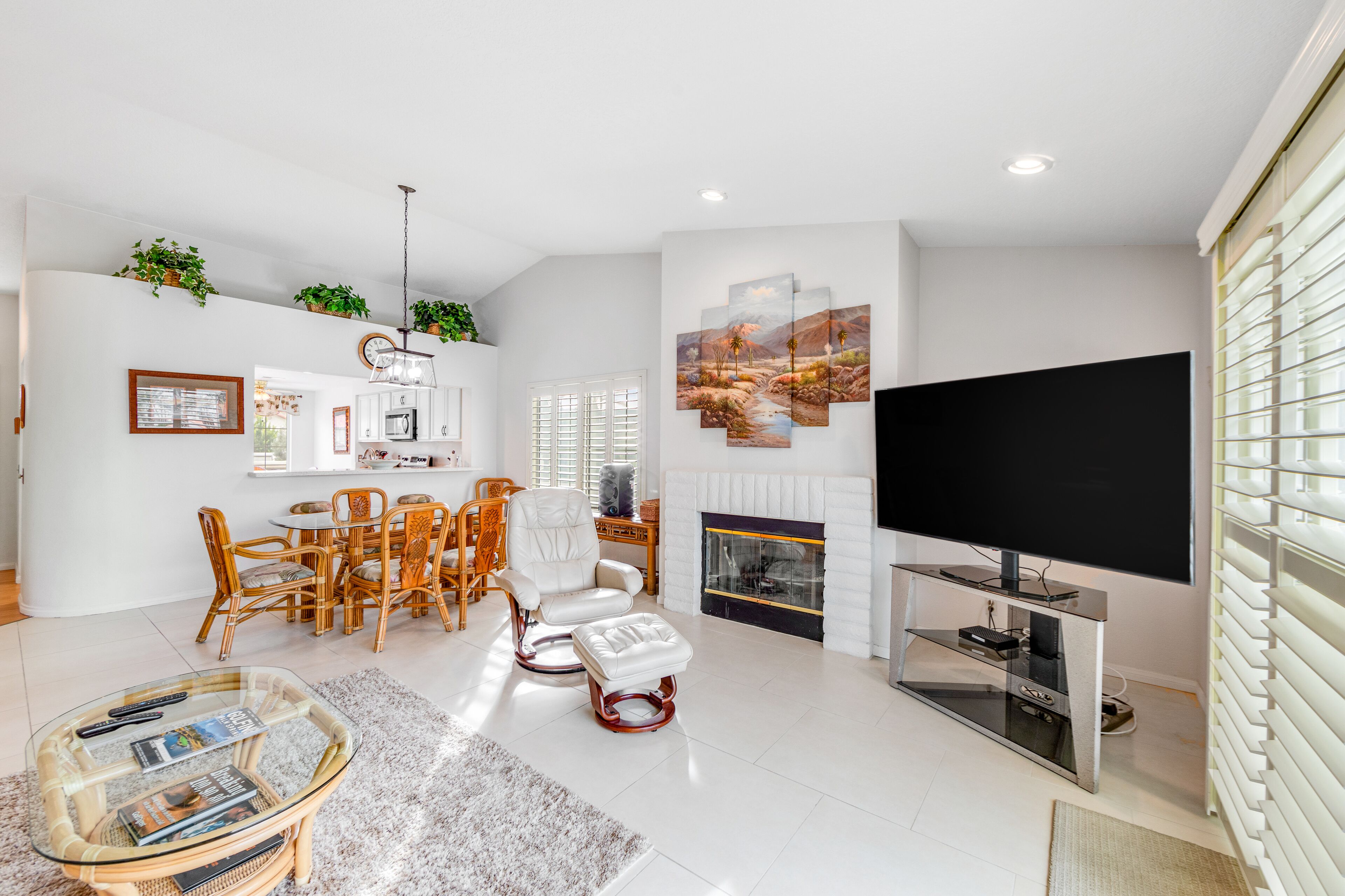 A modern living room with a fireplace, a flat-screen TV, and a dining area with wicker furniture.