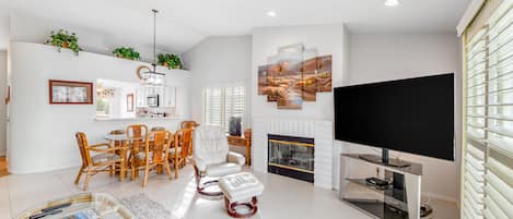 A modern living room with a fireplace, a flat-screen TV, and a dining area with wicker furniture.