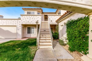 A two-story house with a staircase leading to the front door, a garage, and a well-maintained lawn. - Island-inspired condo with olf course & mountain view & pool access (Palm Desert)