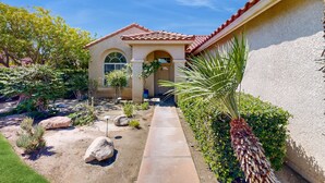 A house with a tiled roof, a paved driveway, and a garden with various plants and a palm tree. - Chic Cathedral City Home with Private Pool & Spa | Minutes to Palm Springs (Cathedral City)