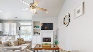 A modern living room with a fireplace, a ceiling fan, and a dining area with a kitchen in the background. - Chic Cathedral City Home with Private Pool & Spa | Minutes to Palm Springs (Cathedral City)