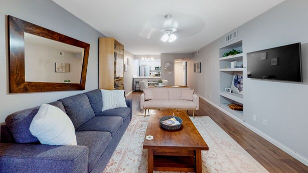 Ein modernes Wohnzimmer mit einem grauen Sofa, einem Holztisch und einem großen Flachbildfernseher an der Wand.