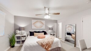 Ein Schlafzimmer mit Bett, Nachttischen, einem Deckenventilator und einem großen Spiegel.