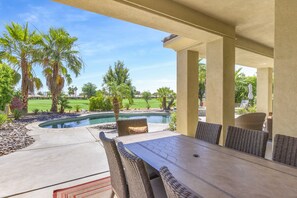 Eine überdachte Terrasse mit Pool, Gartenmöbeln und Blick auf einen Golfplatz.