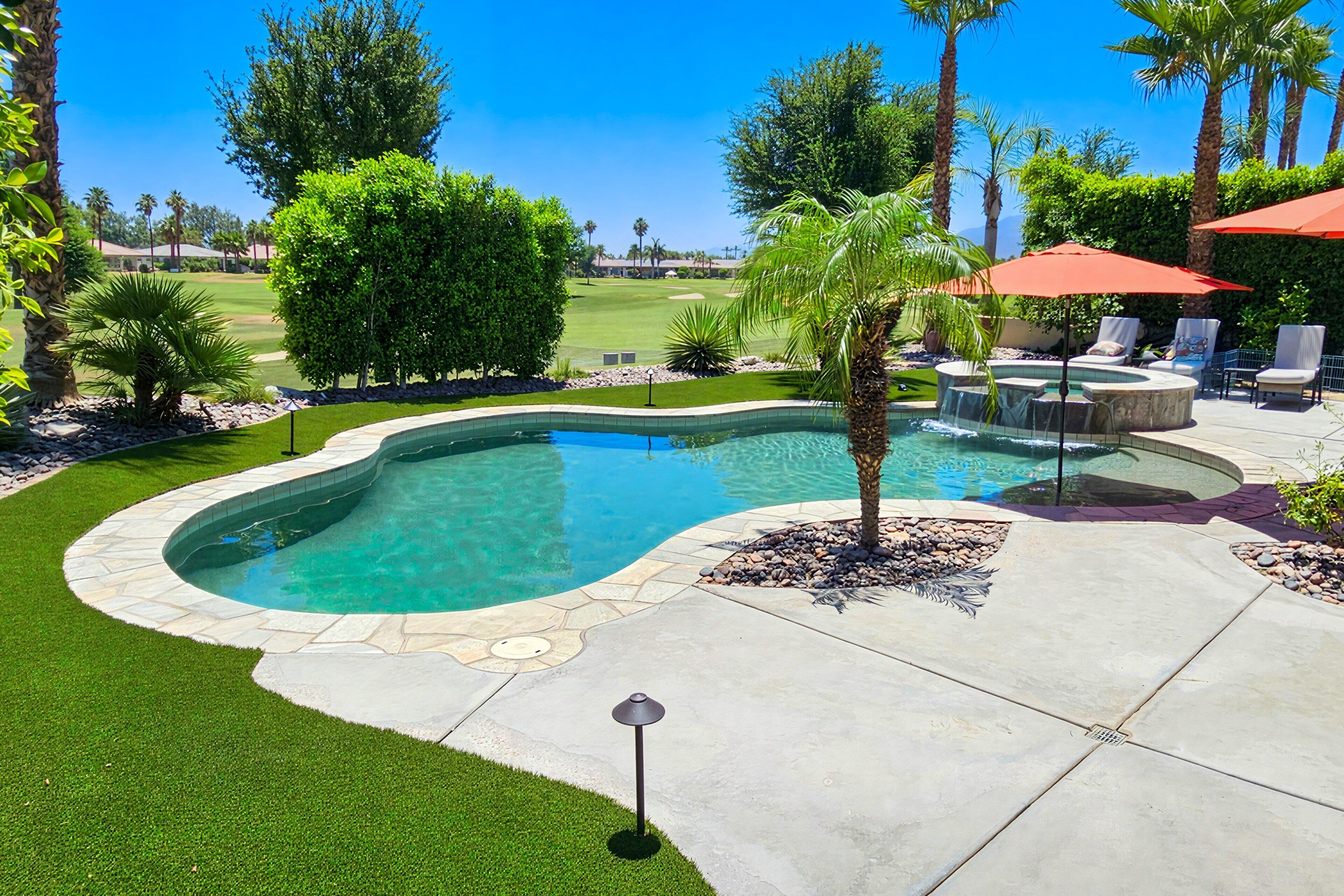 Piscina com borda de pedra, rodeada por um alpendre com cadeiras e guarda-sóis, e vista para um campo de golfe ao fundo.