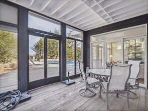 A covered outdoor area with a table and chairs, large windows, and a view of a swimming pool. - Oceanfront 5BR Home w/ Pool | Balcony + Porch View (Bethany Beach)