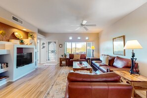 Ein geräumiges Wohnzimmer mit Fernseher, Ledersofas, einem Couchtisch und einem Deckenventilator.