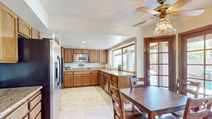 A kitchen with wooden cabinets, a stainless steel refrigerator, a microwave, and a dining area with a table and chairs. - 4 BR house with pool, putting green, great patio (Scottsdale)