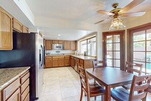 A kitchen with wooden cabinets, a stainless steel refrigerator, a microwave, and a dining area with a table and chairs. - 4 BR house with pool, putting green, great patio (Scottsdale)