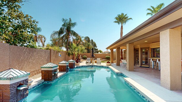 A swimming pool with tiled edges, surrounded by palm trees and a covered patio area with outdoor seating. - 4 BR house with pool, putting green, great patio (Scottsdale)