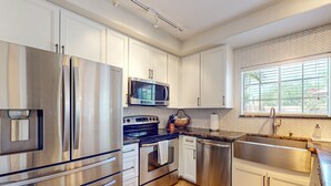 Una cocina moderna con electrodomésticos de acero inoxidable, armarios blancos y un revestimiento de pared con diseño en espiga.