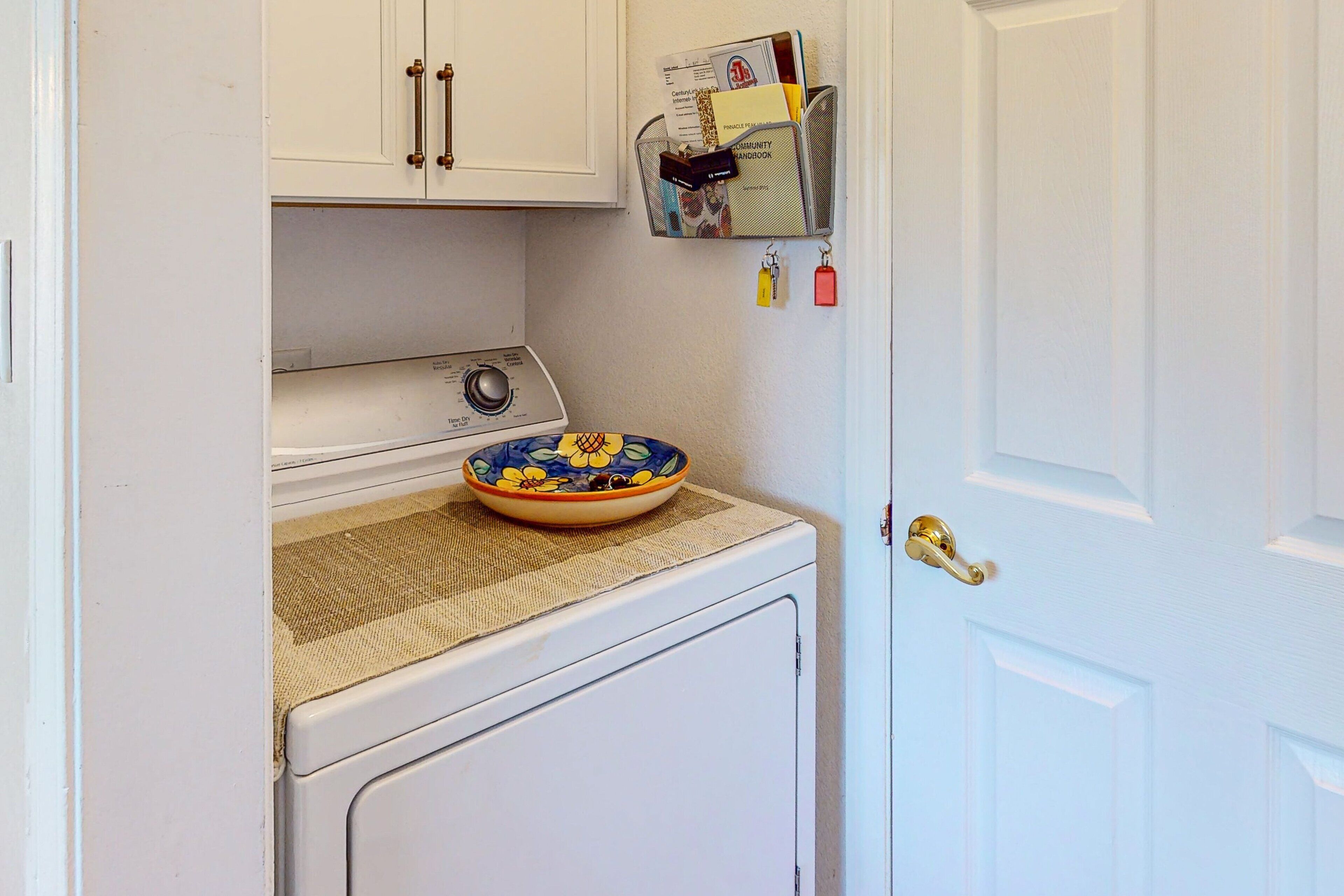 A compact laundry area with a washing machine, a drying rack, and a small shelf with books and keys.