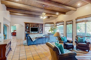 Amplia sala de estar con techo de madera, televisor, sillones de cuero y un ventanal con vista a zonas verdes.