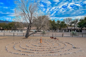 A desert landscape with a circular stone pattern, a tree, and a fenced area.
