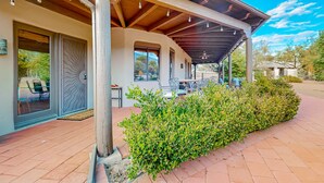 A covered outdoor area with a patio, a wooden pergola, and a well-maintained hedge.