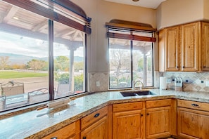 A kitchen with wooden cabinets, a granite countertop, a large window, and a view of a park. - Golf & mountain view desert home with shared pool and gym - dog-friendly (Tucson)