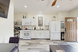 Una cocina moderna con armarios blancos, microondas, estufa y refrigerador. Hay una mesa de comedor con una silla y piso de madera.