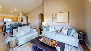 Ein geräumiger Wohnbereich mit grauem Sofa, einem Couchtisch und einem Essbereich, im Hintergrund ist eine Küche zu sehen.