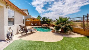 Ein Garten mit Swimmingpool, einer Terrasse mit Stühlen und einem kleinen Wasserfall.