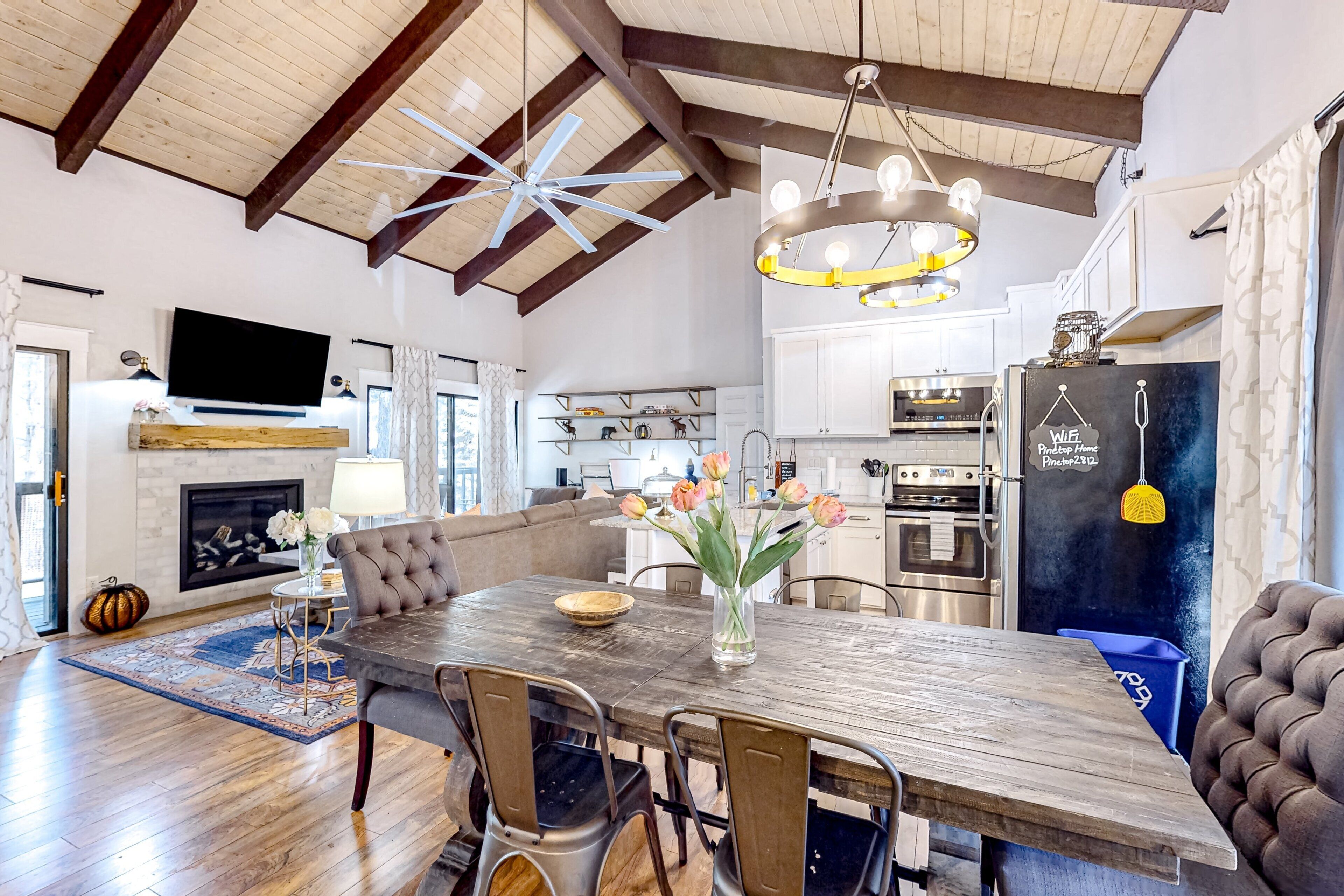 Un salon spacieux avec un plafond haut, une cheminée et un coin repas comprenant une table et des chaises en bois.