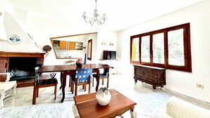 A dining area with a fireplace, wooden furniture, a chandelier, and a large window. - Villa Prestige 🌊✨ - Refinement and Relaxation Just a Step from the Sea (Santa Margherita di Pula)