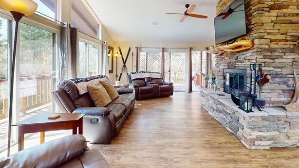 Ein geräumiges Wohnzimmer mit Kamin aus Stein, Ledersofas und Deckenventilator.
