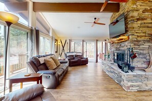 A spacious living room with a stone fireplace, leather sofas, and a ceiling fan. - Shadow Mountain Village Escape | 2 Living Areas, Deck & Yard | Walk to Trail (Flagstaff)