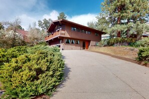 A two-story wooden house with a balcony, surrounded by dense greenery and a clear sky. - Shadow Mountain Village Escape | 2 Living Areas, Deck & Yard | Walk to Trail (Flagstaff)