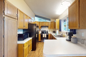 A kitchen with wooden cabinets, a refrigerator, stove, microwave, and a large island with a sink. - Shadow Mountain Village Escape | 2 Living Areas, Deck & Yard | Walk to Trail (Flagstaff)