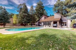 Une maison moderne avec une piscine, entourée d’une pelouse bien entretenue et de grands arbres.