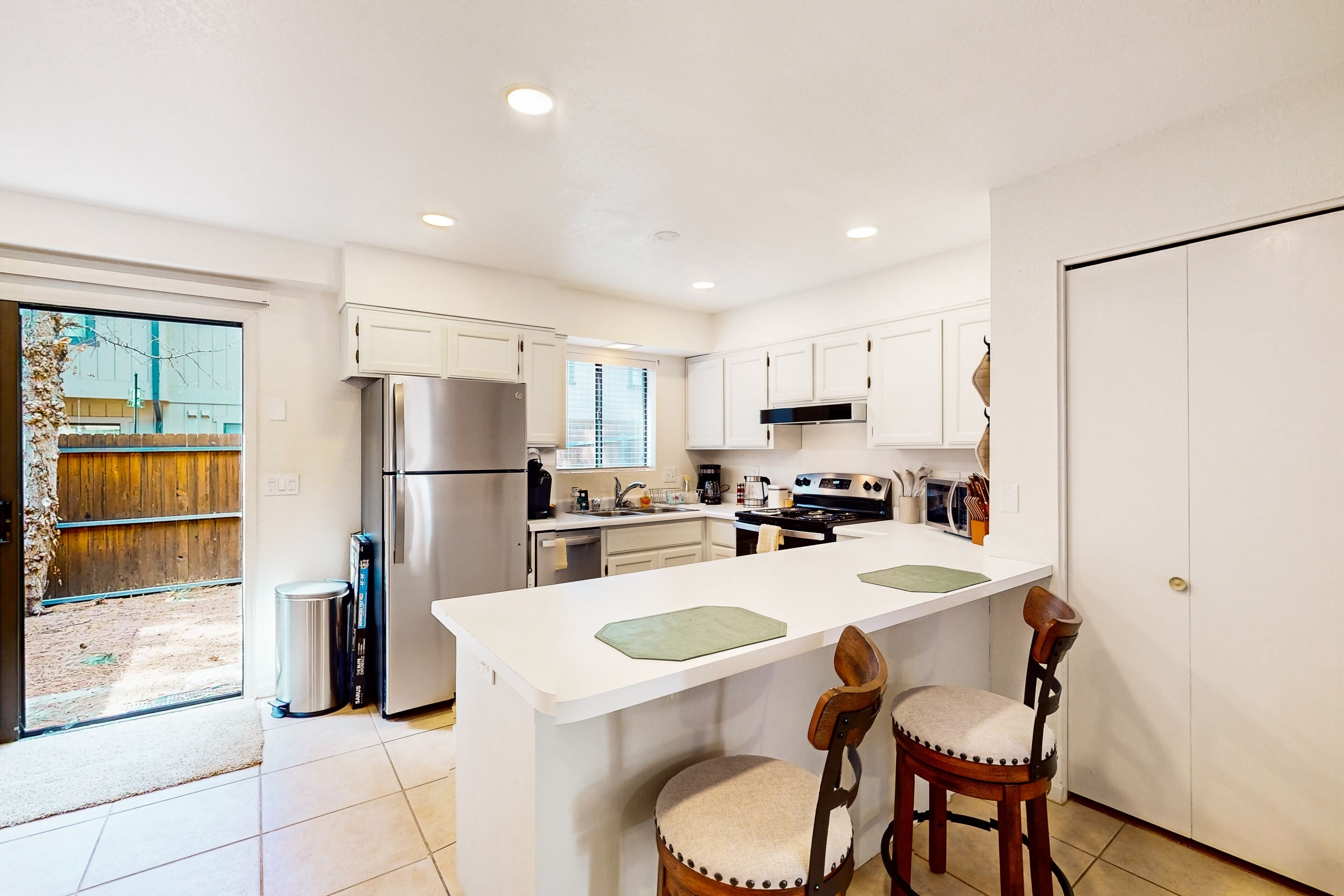 A modern kitchen with white cabinets, a stainless steel refrigerator, a gas stove, and a large island with bar stools.