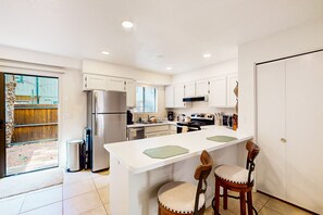 A modern kitchen with white cabinets, a stainless steel refrigerator, a gas stove, and a large island with bar stools. - Peaceful condo with patio, pool/hot tub, gym, and fireplace (Pinetop-Lakeside)